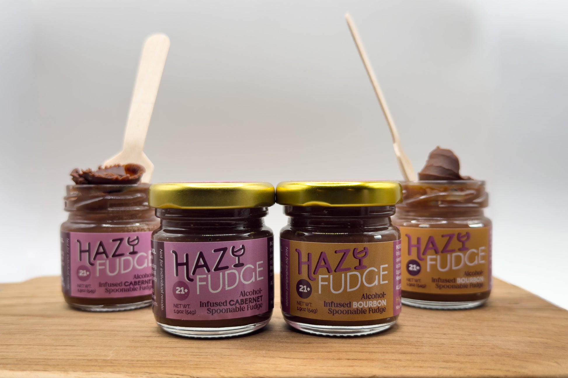 Four jars of Hazy Fudge on a wooden surface with a white background